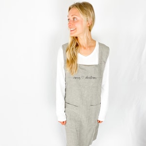 May include: A gray and white striped apron with the text "merry christmas" embroidered on the front. The apron has two pockets and adjustable straps.