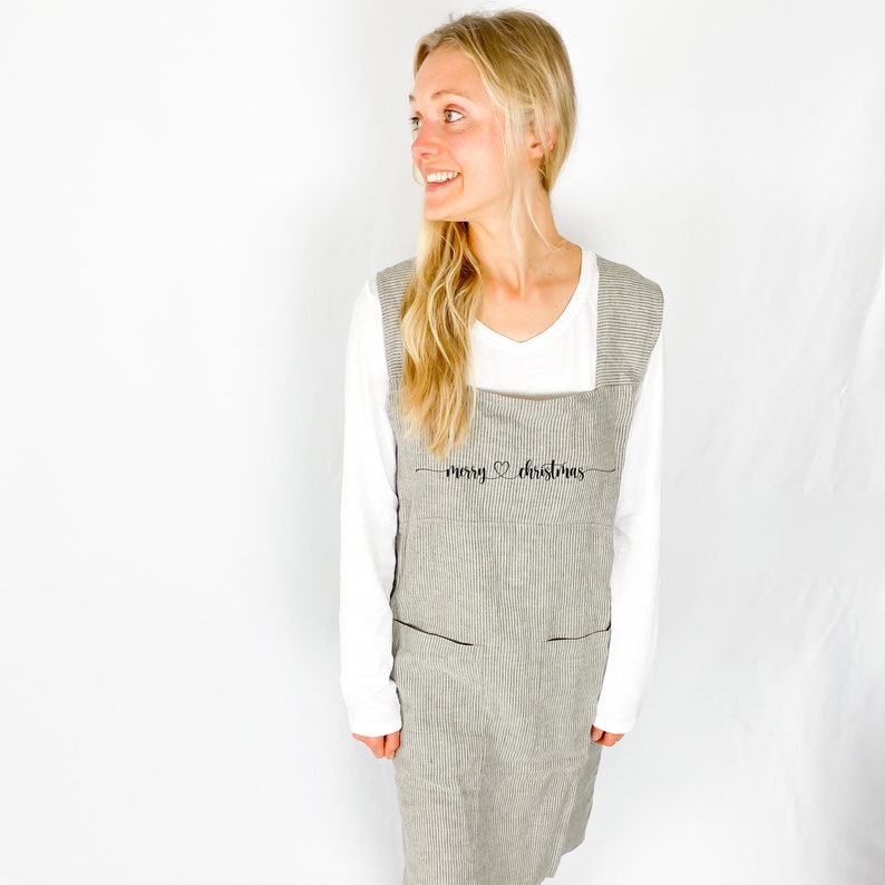 May include: A gray and white striped apron with the text "merry christmas" embroidered on the front. The apron has two pockets and adjustable straps.