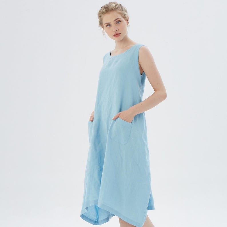 May include: A light blue sleeveless linen dress with a scoop neck and two pockets. The dress has a relaxed fit and a slightly asymmetrical hem.
