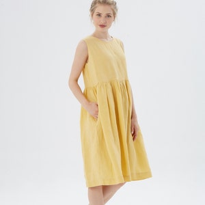 May include: A sleeveless, yellow linen dress with a gathered waist and pockets. The dress falls to the mid-calf and has a simple, round neckline. The fabric appears to be lightweight and breathable, suitable for warm weather. The dress is a solid color.