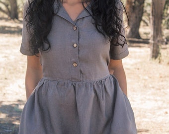 May include: A gray linen dress with a collared neckline and button closure. The dress has short sleeves and a gathered skirt.