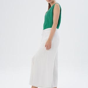 May include: A sleeveless emerald green top paired with white wide-leg trousers featuring a side tie closure. The outfit consists of a solid green tank top and loose-fitting white pants that reach the ankles, presented in a simple, clean style.