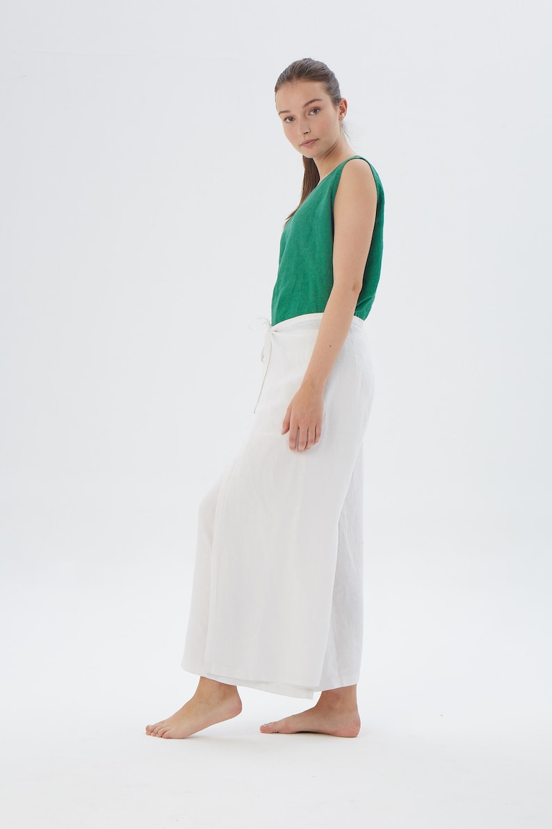May include: A sleeveless emerald green top paired with white wide-leg trousers featuring a side tie closure. The outfit consists of a solid green tank top and loose-fitting white pants that reach the ankles, presented in a simple, clean style.