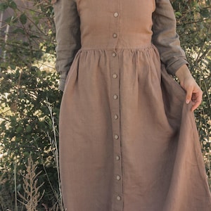 May include: A brown linen dress with long sleeves and a button-down front. The dress has a fitted bodice and a flowing skirt. The sleeves are a lighter shade of brown. The dress is made of a soft, natural fabric.