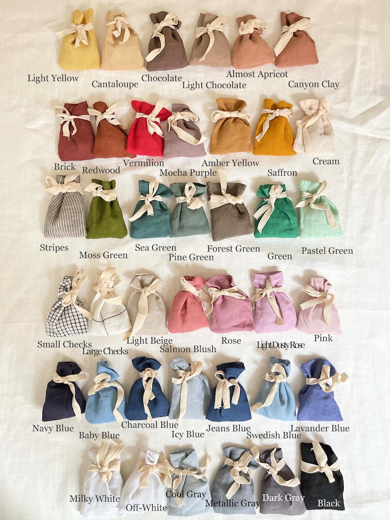 May include: A collection of small fabric drawstring pouches arranged in rows, each tied with a cream-colored ribbon. The pouches come in a wide variety of solid colors, including yellow, red, blue, green, gray, and black, along with several patterned options.