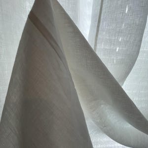 a close-up view of a white fabric, possibly a piece of clothing or a sheer curtain, with a soft, flowing texture.