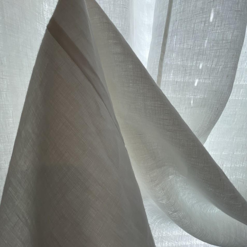 a close-up view of a white fabric, possibly a piece of clothing or a sheer curtain, with a soft, flowing texture.