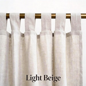 May include: A light beige curtain panel featuring a tab top header design. The fabric has a visible woven texture and hangs from a metallic gold curtain rod. The text Light Beige is printed in a dark brown serif font at the bottom center.