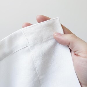 A hand is holding a white fabric, possibly a piece of clothing or a textile, with the fabric folded in half.