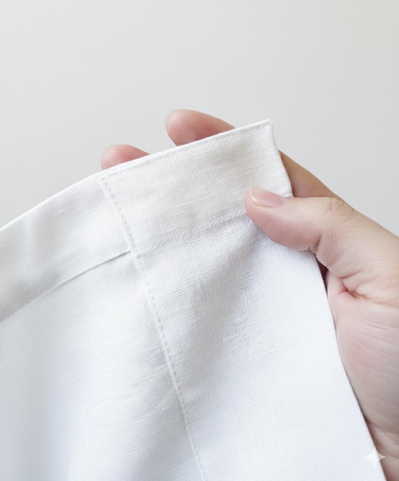 A hand is holding a white fabric, possibly a piece of clothing or a textile, with the fabric folded in half.