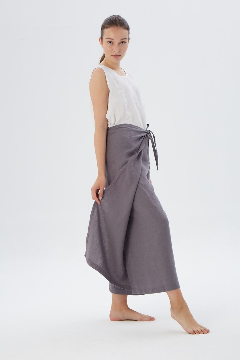 Puede incluir: Una mujer con una camiseta sin mangas blanca y pantalones envolventes grises. Los pantalones se atan a la cintura con una cinta de tela a juego. El conjunto es de tejido ligero, adecuado para el clima c&aacute;lido. Los pantalones miden unos 100 cm de largo.