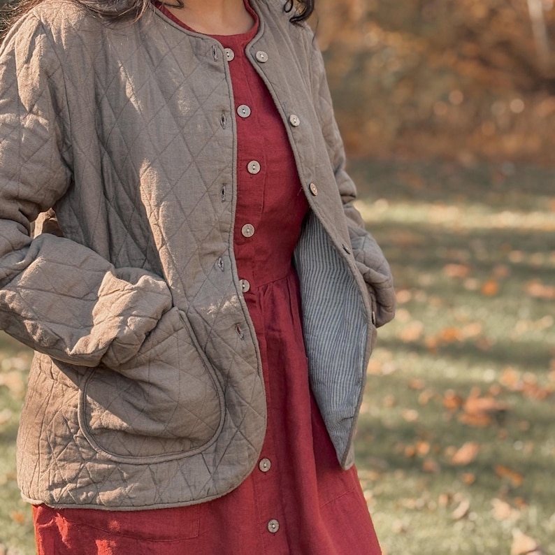 Puede incluir: Chaqueta acolchada verde oliva con cuello redondo y botones. La chaqueta se lleva sobre un vestido rojo con detalles de botones. El forro de la chaqueta es de tela a rayas azul claro y blanco. El conjunto es adecuado para el oto&ntilde;o.