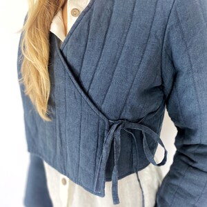 May include: A dark blue quilted wrap jacket with a tie closure. The jacket is cropped and has a relaxed fit.