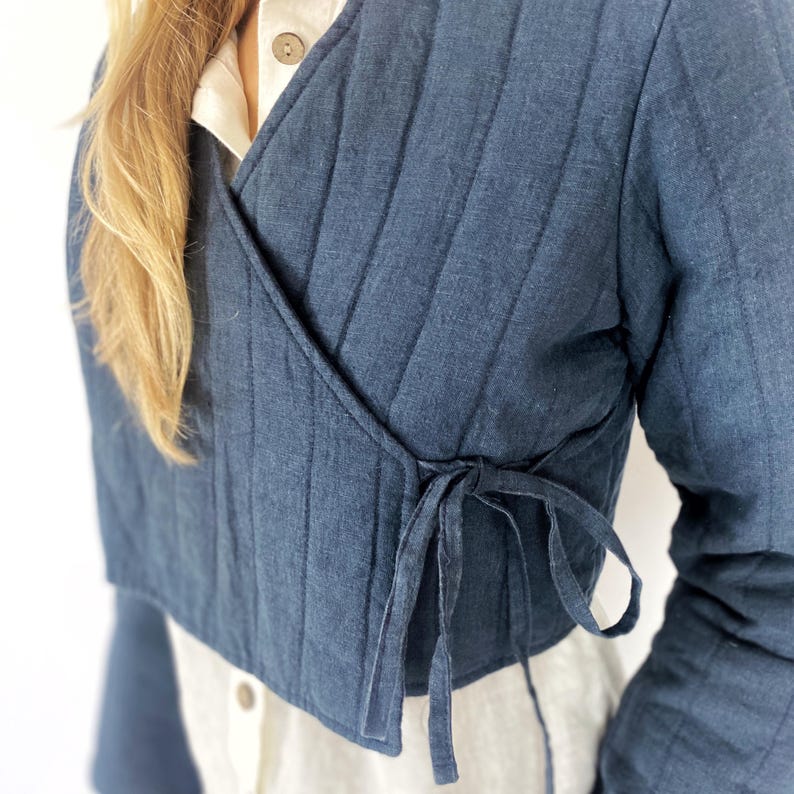 May include: A dark blue quilted wrap jacket with a tie closure. The jacket is cropped and has a relaxed fit.