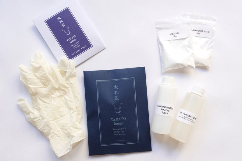 Puede incluir: Un kit de tinte indigo natural con instrucciones, guantes, soda ash, hidrosulfito de sodio, fijador y vinagre. El kit incluye un sobre azul con el texto "大和藍" y "YAMATO Indigo" en blanco.