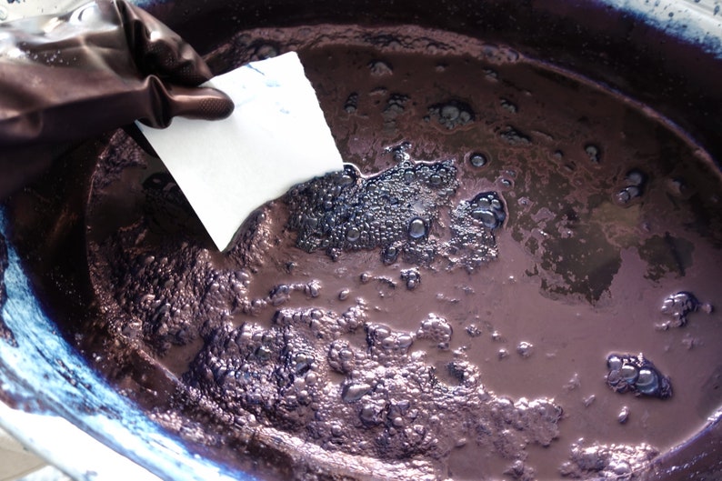 Puede incluir: Primer plano de un cuenco de cer&aacute;mica blanca lleno de un l&iacute;quido morado oscuro. El l&iacute;quido tiene una consistencia espesa y viscosa y est&aacute; cubierto de peque&ntilde;as burbujas. Una mano enguantada sostiene una toalla de papel blanca sobre el l&iacute;quido.