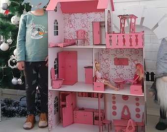 Peut inclure: Une grande maison de poupée rose à plusieurs étages avec des éléments intérieurs détaillés, notamment des meubles et du papier peint. La maison de poupée a un toit en pente et un balcon. Deux poupées sont assises à l'intérieur. La maison de poupée est en bois.