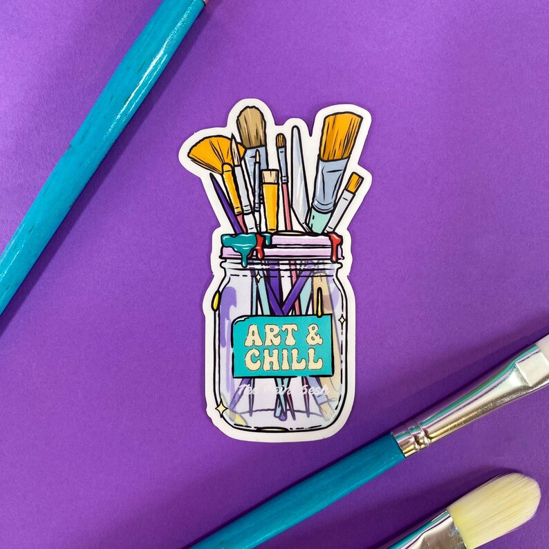 Puede incluir: Una pegatina de un tarro de cristal lleno de pinceles. El tarro tiene una etiqueta turquesa con el texto "ART & CHILL" en amarillo y blanco.