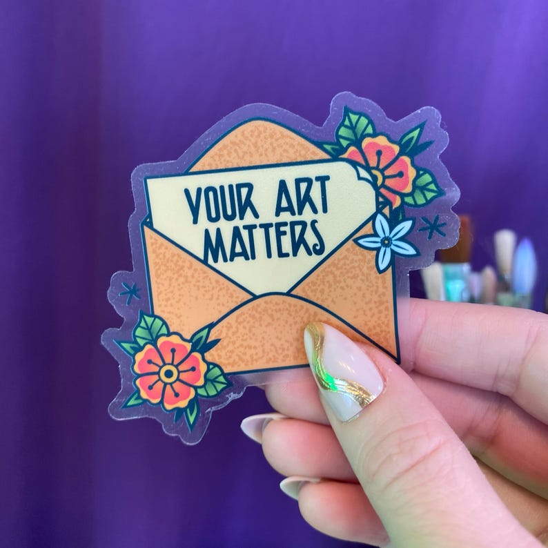 Op de afbeelding: Een transparante sticker met een lichtoranje envelop met de tekst "YOUR ART MATTERS" erin. De envelop is versierd met bloemen in tinten rood, oranje, geel en groen.