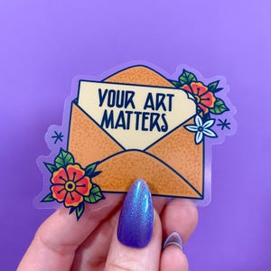 Op de afbeelding: Een transparante sticker met een gele envelop met de tekst "YOUR ART MATTERS" erin. De envelop is versierd met bloemen in rood, oranje, wit en groen.