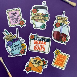 Op de afbeelding: Negen kleurrijke stickers met verschillende zinnen en ontwerpen. De stickers bevatten zinnen zoals "Bad Art is Good Art", "Shhh... Coffee & Weed First", "Aww Fuck!", "Don't Drink Paint Water", "Notice Break All The Rules", "Your Art Matters", en "You're Doing Great!" De stickers zijn versierd met bloemmotieven en hebben een vintage esthetiek.