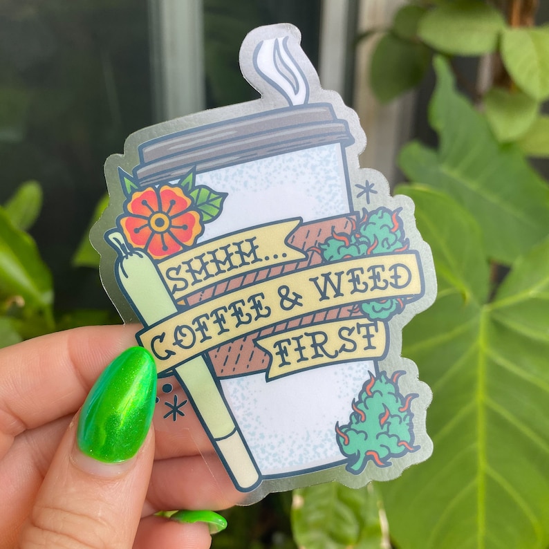 May include: A clear sticker with a cartoon illustration of a coffee cup, a joint, and a green leafy plant. The text reads "SMMH... COFFEE & WEED FIRST".
