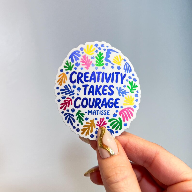 May include: A circular sticker with a scalloped edge featuring the blue text "CREATIVITY TAKES COURAGE -MATISSE" in the center. The design is surrounded by a colorful pattern of abstract organic leaf-like shapes in yellow, pink, green, and blue.