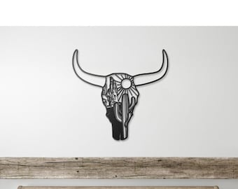May include: A black metal wall sculpture of a bull skull with a cactus and sun design. The sculpture is hanging above a wooden bed frame with white bedding and a wooden bench.