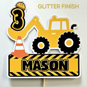 K&ouml;nnte beinhalten: Gelber Baumaschinen-Kuchentopper mit einer schwarzen Zahl 3, einem Baukegel und dem Namen "MASON" auf einem gelb-schwarz gestreiften Schild. Der Topper hat eine Glitzer-Oberfl&auml;che.