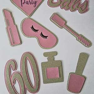 May include: Pink and gold glitter paper cutouts for a pamper party. The cutouts include the words "Pamper Party", "Babs", and the number "60". Other cutouts include a lipstick, eye mask, perfume bottle, and nail polish.