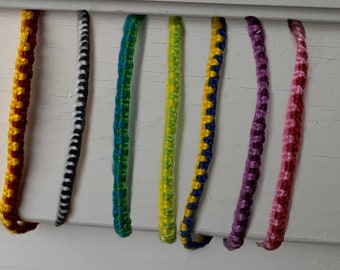 May include: Eight colorful friendship bracelets made with woven string. The bracelets are in the colors yellow, black, green, yellow, blue, purple, pink, and red.