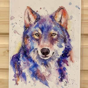 May include: Watercolour painting of a wolf's face in shades of blue, purple and brown. The wolf has a gentle expression and is surrounded by white splashes of paint.