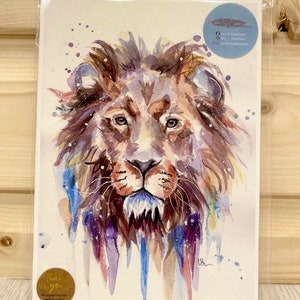May include: Watercolor painting of a lion's face with a blue, purple, and brown color scheme. The lion's face is in focus, and the background is a white canvas with splatters of paint.