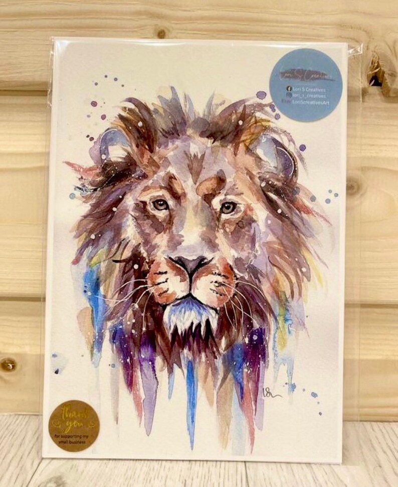 May include: Watercolor painting of a lion's face with a blue, purple, and brown color scheme. The lion's face is in focus, and the background is a white canvas with splatters of paint.
