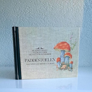 Könnte beinhalten: Ein niederländischsprachiges Buch mit dem Titel "Paddestoelen" mit einer Illustration von Pilzen mit orangefarbenen und blauen Kappen. Das Cover hat eine beige Leinenstruktur. Der Buchrücken ist dunkelgrün. Der Text auf dem Cover lautet "Readers Digest Veldgids voor de Natuurliefhebber".