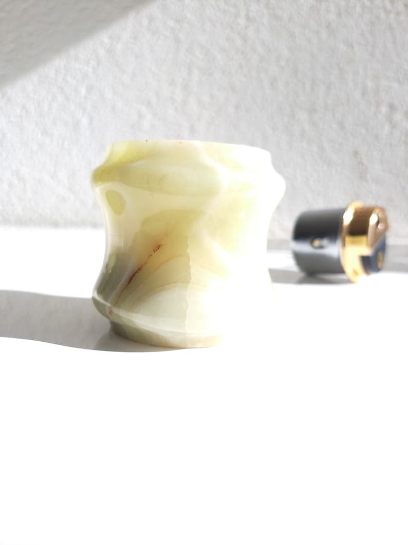May include: A light green, white, and brown marble ring holder with a unique, faceted design.
