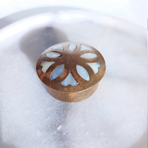 May include: A small, round, brass trinket box with a decorative, openwork design featuring a white, mother-of-pearl inlay. The box has a slightly aged, antique look.