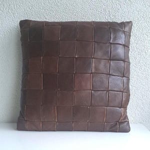 Può includere: Un cuscino in pelle marrone con un design trapuntato. Il cuscino è composto da diversi quadrati di pelle cuciti insieme.