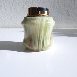 May include: A green and gold table lighter made of onyx with a black top.