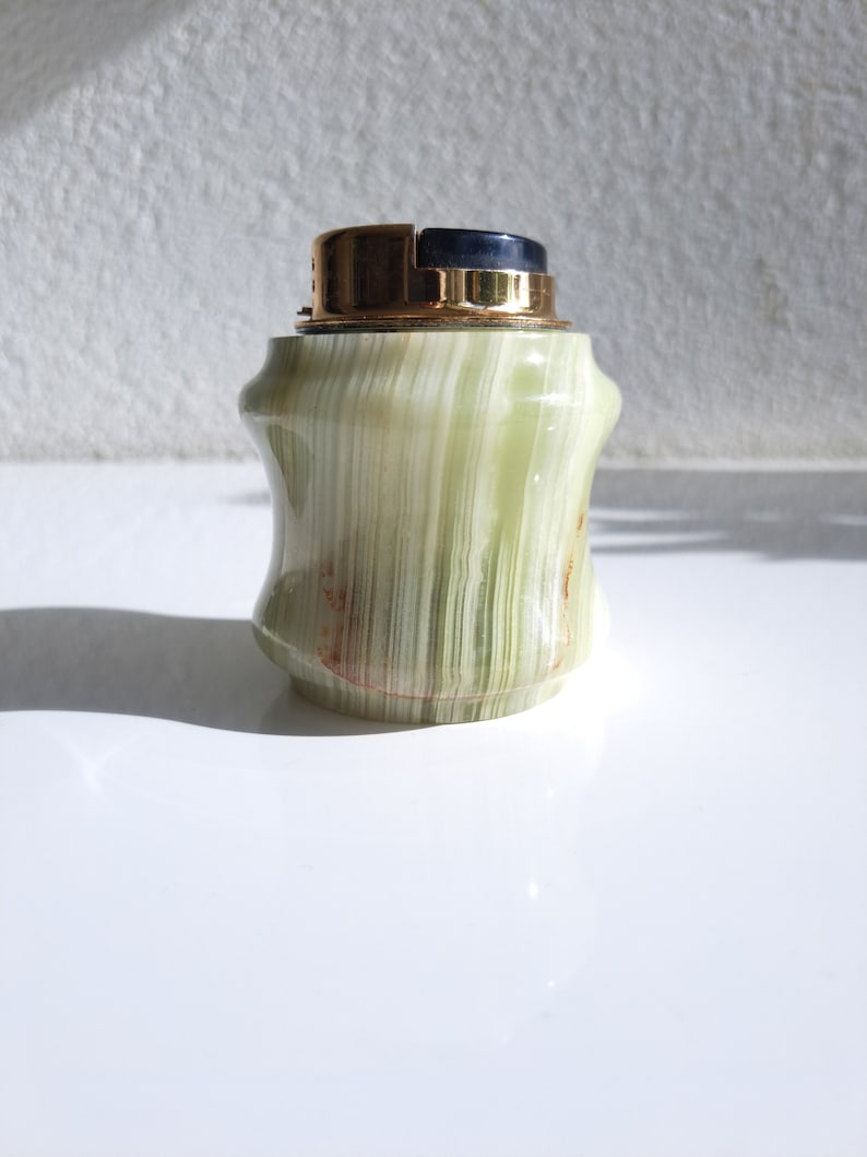 May include: A green and gold table lighter made of onyx with a black top.