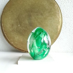 Peut inclure: Un presse-papier en verre vert avec des tourbillons blancs et des bulles d'air à l'intérieur. Le presse-papier a la forme d'un œuf.