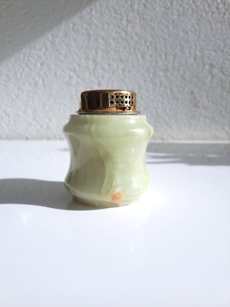 May include: A green marble bottle stopper with a gold top. The bottle stopper has a textured surface and a round shape.