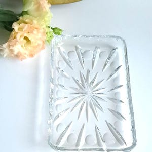 Könnte beinhalten: Eine rechteckige Glasschale aus klarem Glas mit einem Sternmuster und einem erhöhten Rand. Die Schale ist perfekt zum Servieren von Snacks oder Vorspeisen.