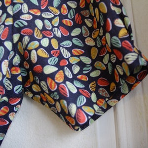 May include: Close-up of a dark blue fabric with a colorful pattern of small, teardrop-shaped designs. The fabric has a slightly textured surface.