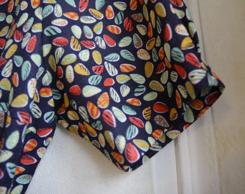 May include: Close-up of a dark blue fabric with a colorful pattern of small, teardrop-shaped designs. The fabric has a slightly textured surface.