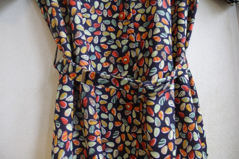 May include: A navy blue dress with a colorful abstract print of small, teardrop-shaped patterns. The dress has a belt and buttons.