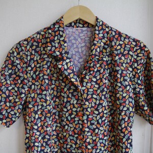 May include: A short-sleeved button-up shirt with a dark blue background and a colorful pattern of small, abstract shapes.