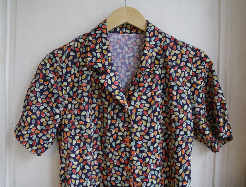 May include: A short-sleeved button-up shirt with a dark blue background and a colorful pattern of small, abstract shapes.