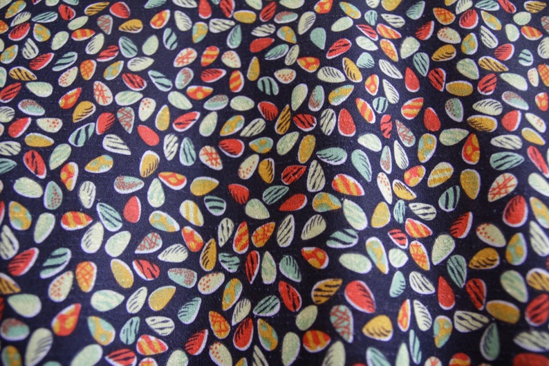 May include: A dark blue fabric with a repeating pattern of colorful, abstract shapes resembling seeds or leaves. The shapes are in shades of red, yellow, green, and white.