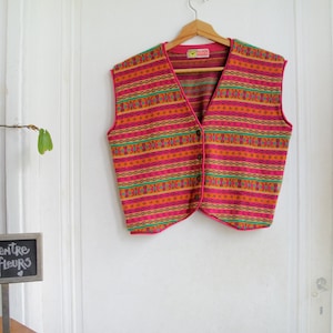 May include: A pink, orange, green, and yellow patterned vest with a button closure. The vest has a pink trim and a small label that says "Folk House".